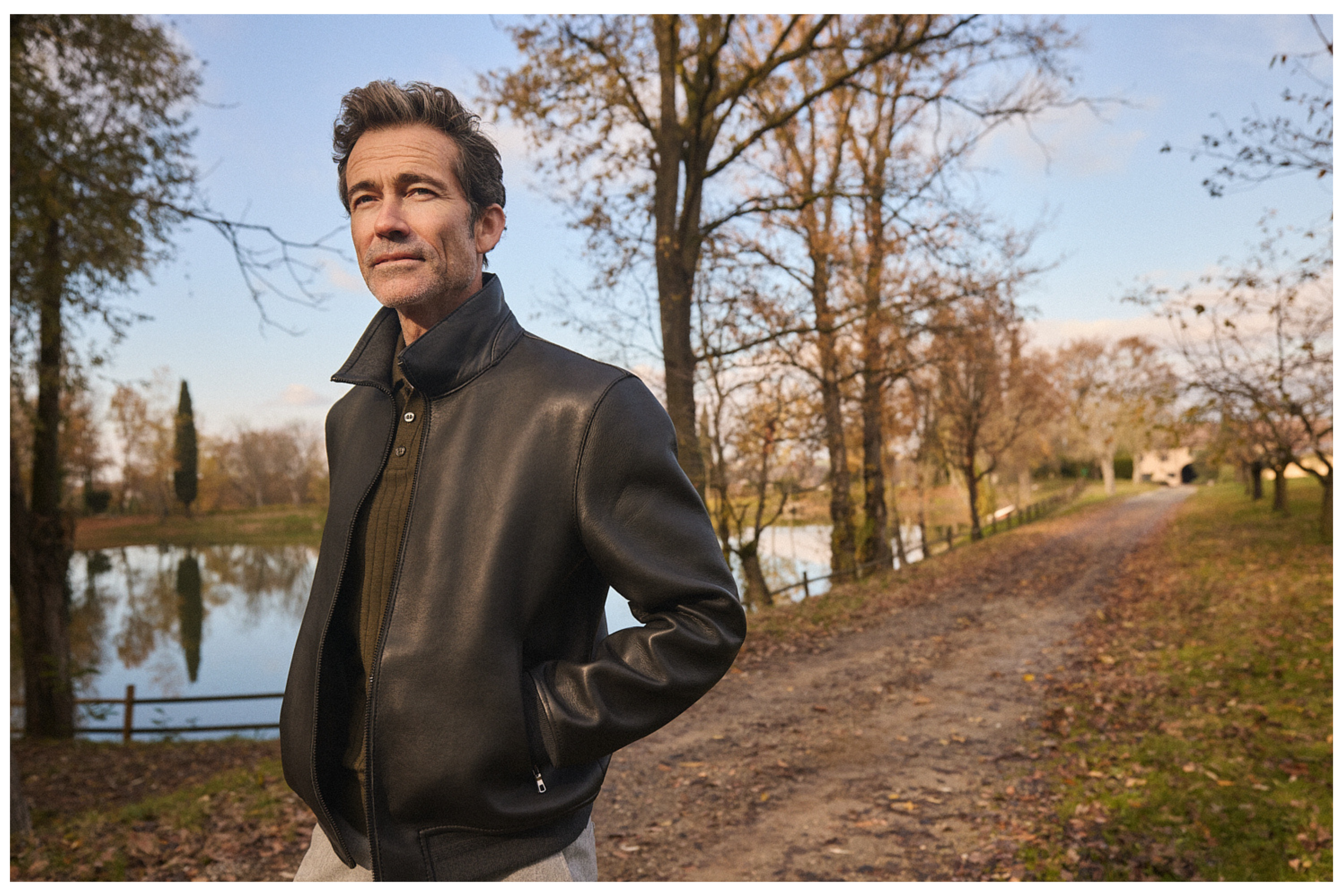 Άνδρας με δερμάτινο jacket Portobello’s στέκεται δίπλα σε λίμνη στο Roncolo, αποπνέοντας ήρεμη, φθινοπωρινή κομψότητα.