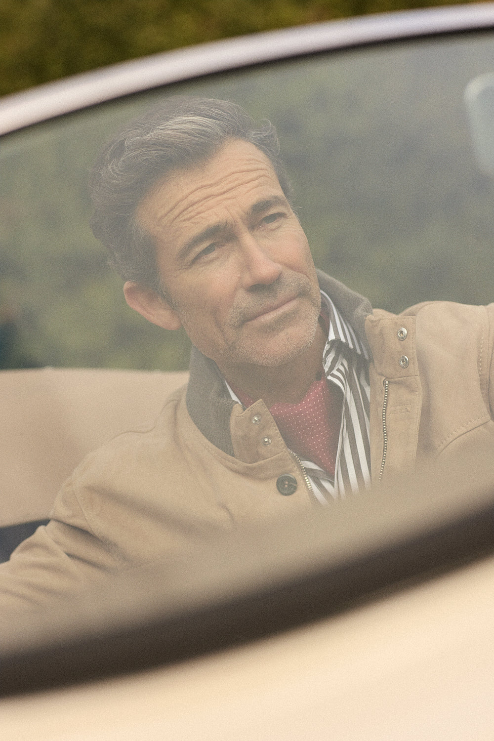 Άνδρας με καφέ jacket, ριγέ πουκάμισο και γραβάτα Portobello’s σε κινηματογραφικό σκηνικό μέσα από αυτοκίνητο.