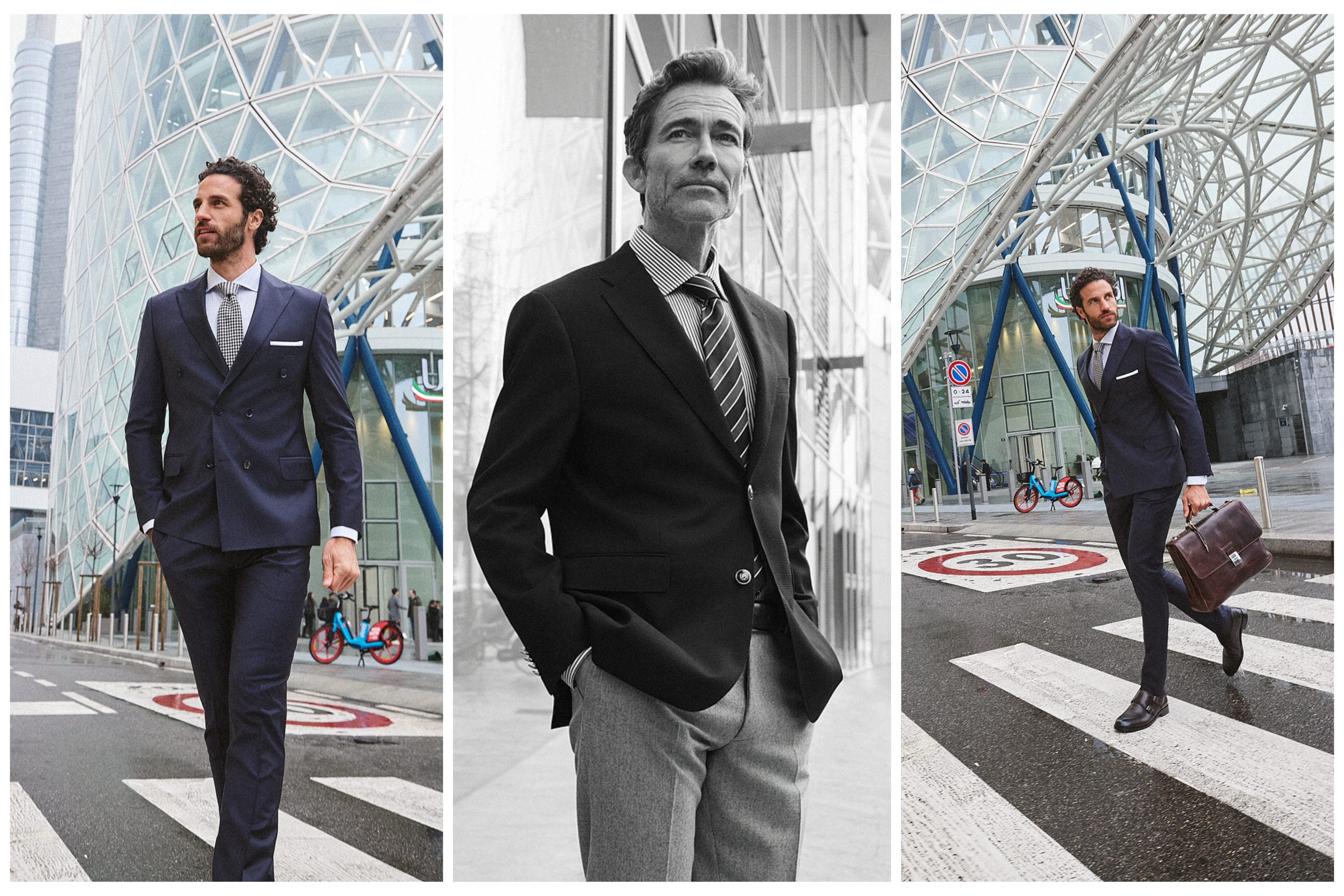 Τρεις άνδρες με κοστούμια Portobello' s περπατούν με αυτοπεποίθηση στο Μιλάνο, ανάμεσα σε σύγχρονα γυάλινα κτίρια και διαβάσεις πεζών. Ο ένας κρατά χαρτοφύλακα, ενώ ένας δεύτερος με ασπρόμαυρο look στέκεται μπροστά σε ανακλαστική γυάλινη πρόσοψη.