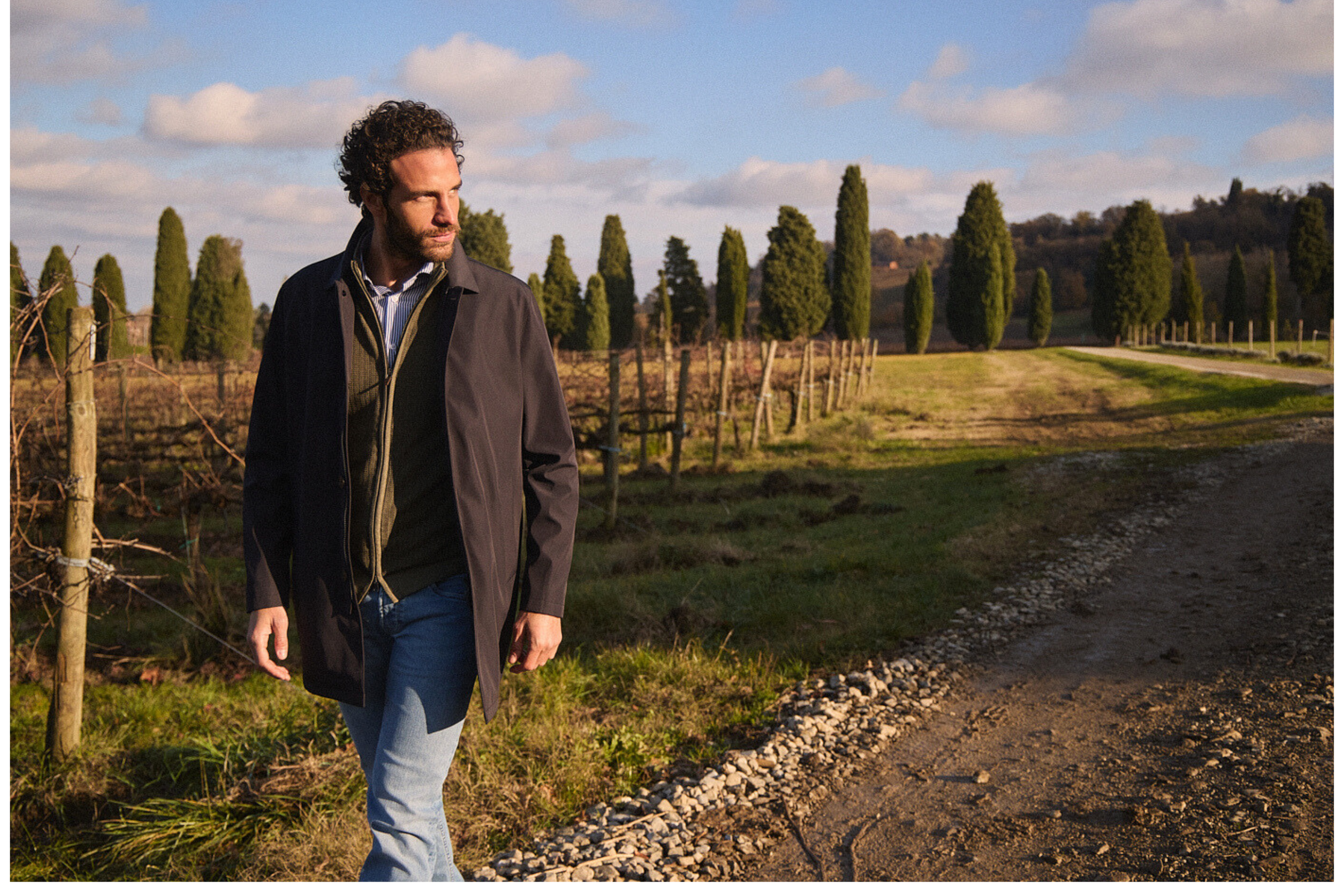 Άνδρας περπατά σε αμπελώνα φορώντας παλτό Portobello’s, σε αγροτικό τοπίο κοντά στο Roncolo με καθαρό φθινοπωρινό ουρανό.
