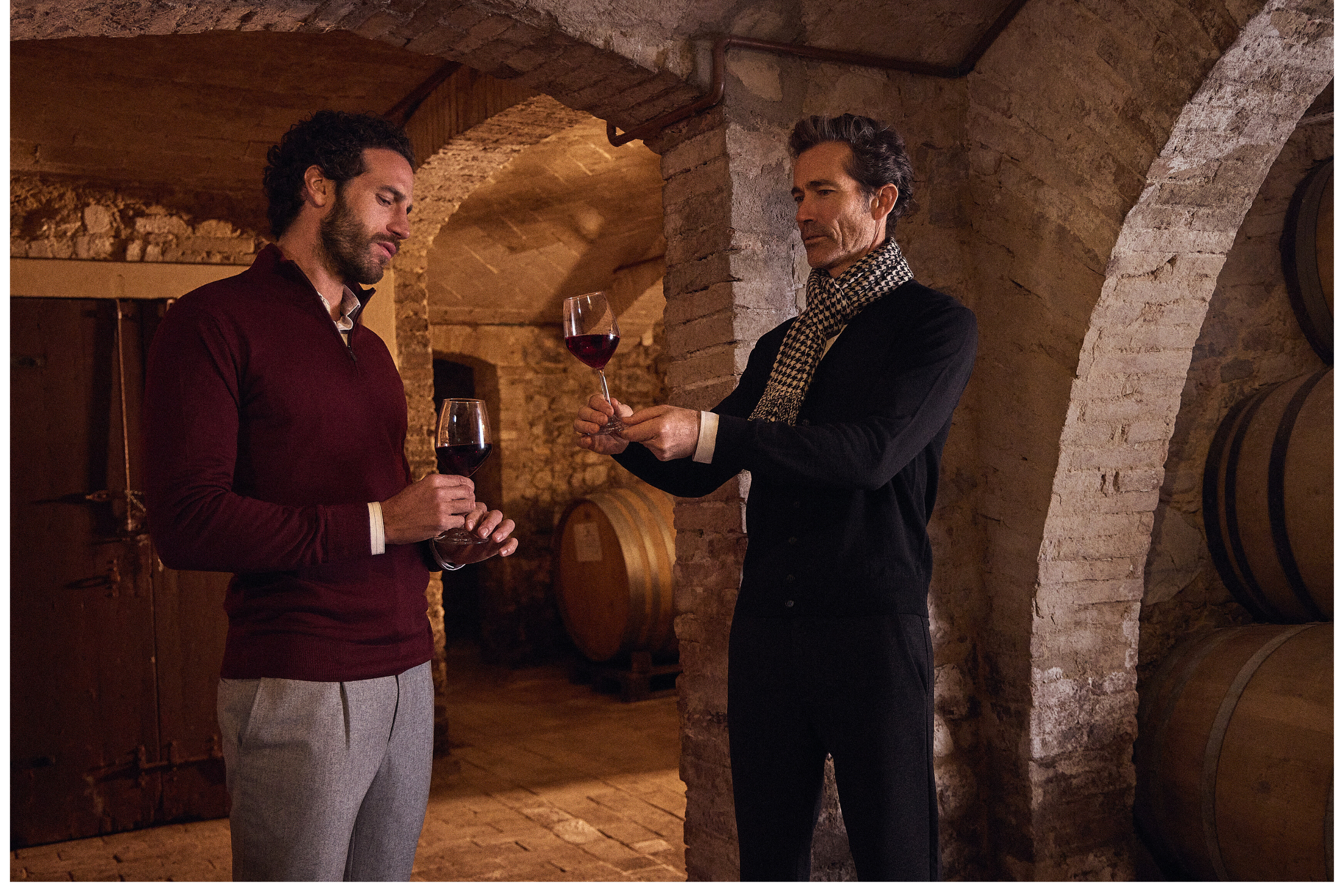 Δύο άνδρες φοράνε ρούχα Portobello's και δοκιμάζουν κόκκινο κρασί σε κελάρι.